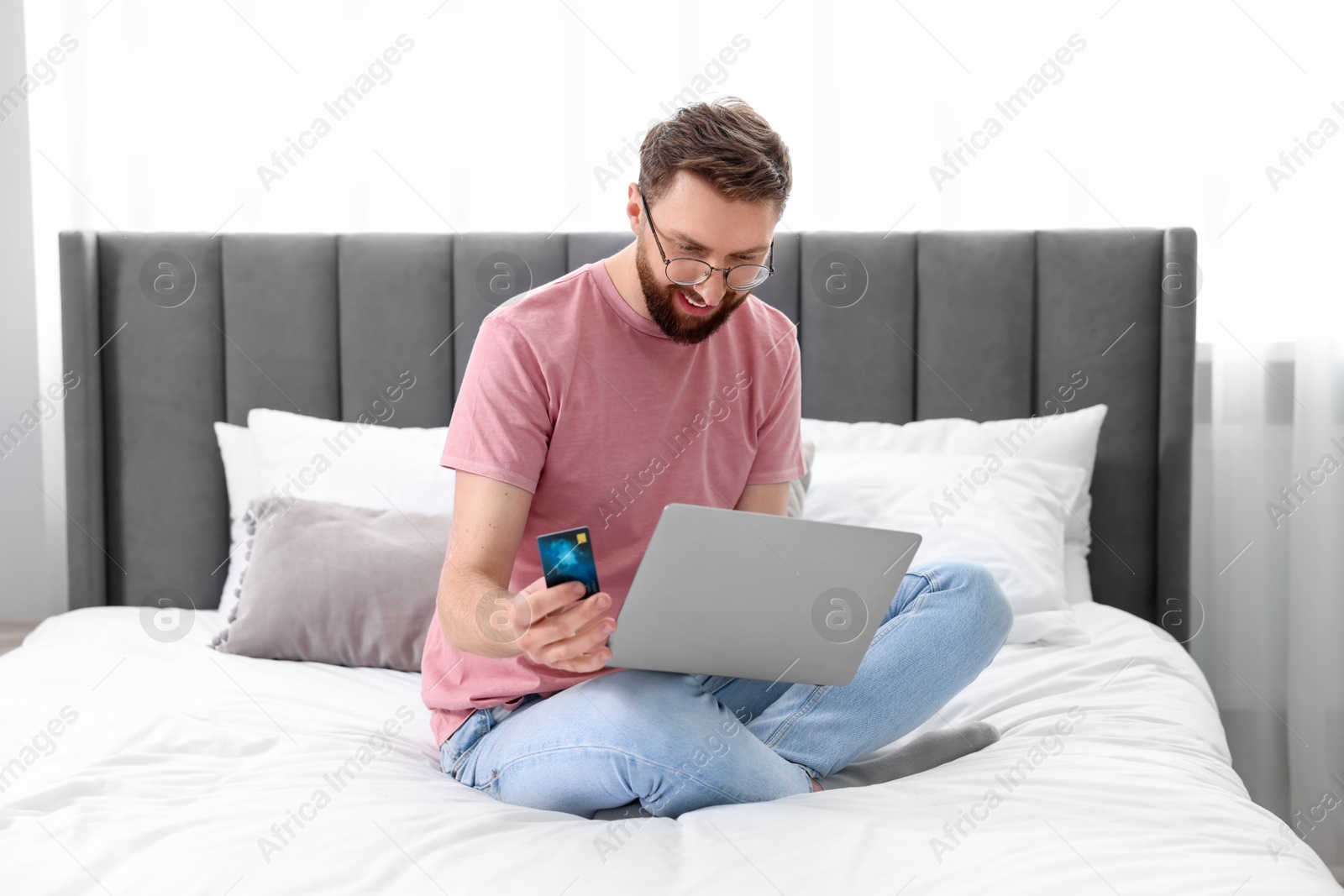 Photo of Online banking. Happy young man with credit card and laptop paying purchase at home