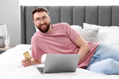 Photo of Online banking. Happy young man with credit card and laptop paying purchase at home