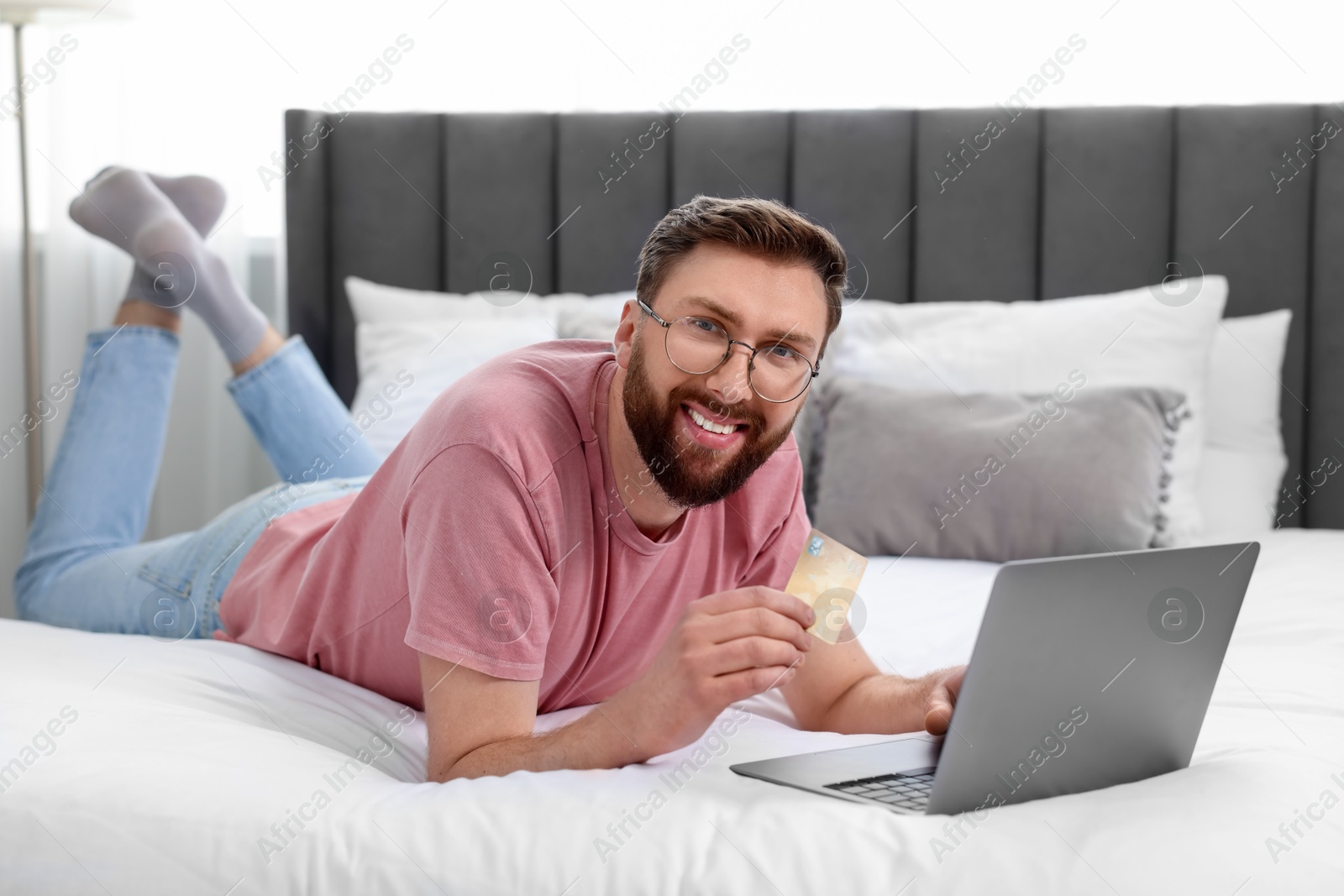 Photo of Online banking. Happy young man with credit card and laptop paying purchase at home