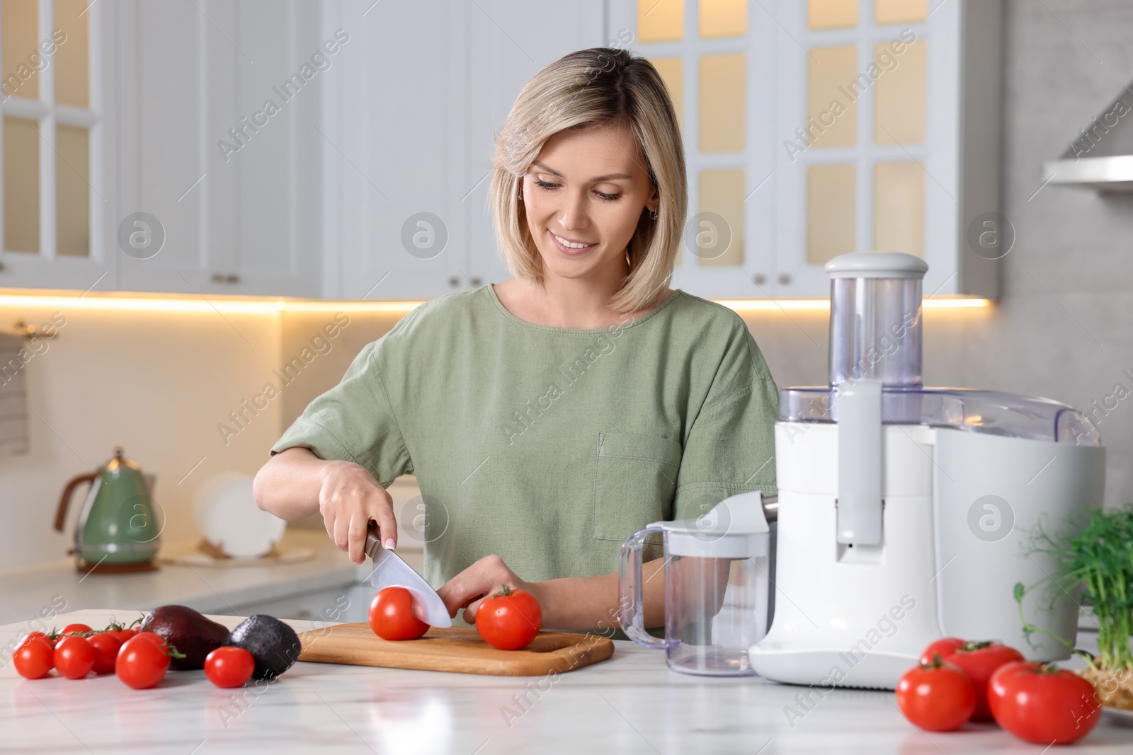 Photo of Juicer and fresh products on white marble table. Smiling woman cutting tomato in kitchen