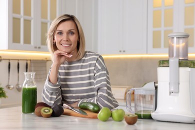 Smiling woman with juicer and fresh products at white marble table in kitchen