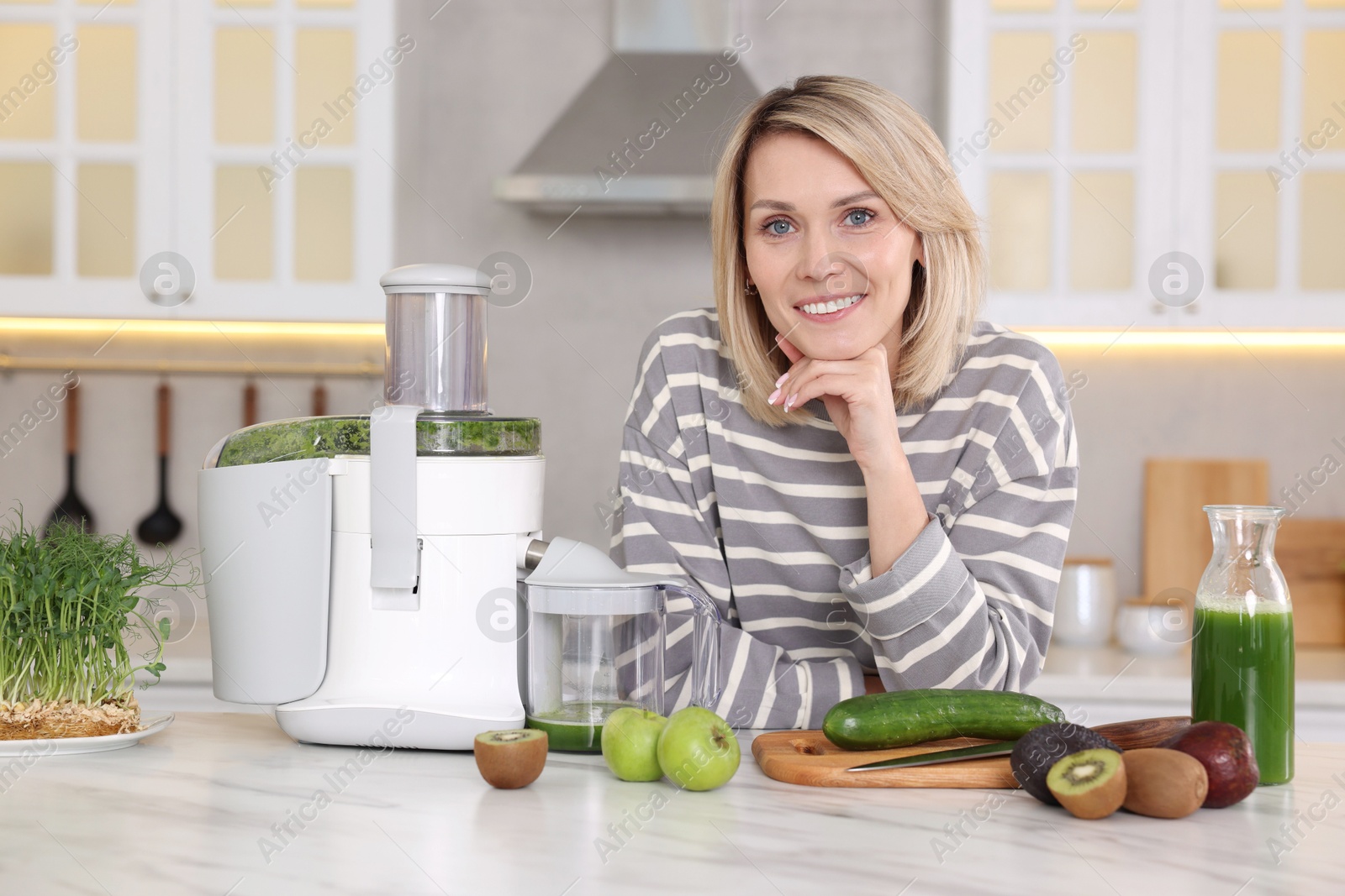 Photo of Smiling woman with juicer and fresh products at white marble table in kitchen