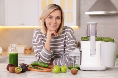 Photo of Smiling woman with juicer and fresh products at white marble table in kitchen