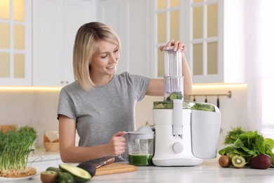 Smiling woman with fresh products using juicer at white marble table in kitchen