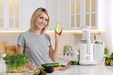 Smiling woman with juicer and fresh products at white marble table in kitchen