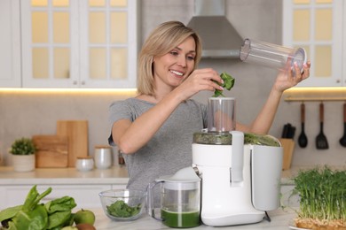 Photo of Smiling woman putting fresh basil into juicer at white marble table in kitchen