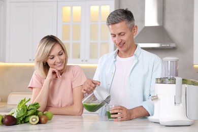 Happy couple with juicer, fresh products and tasty juice at white marble table in kitchen