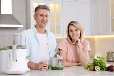 Photo of Happy couple with juicer, fresh products and tasty juice at white marble table in kitchen