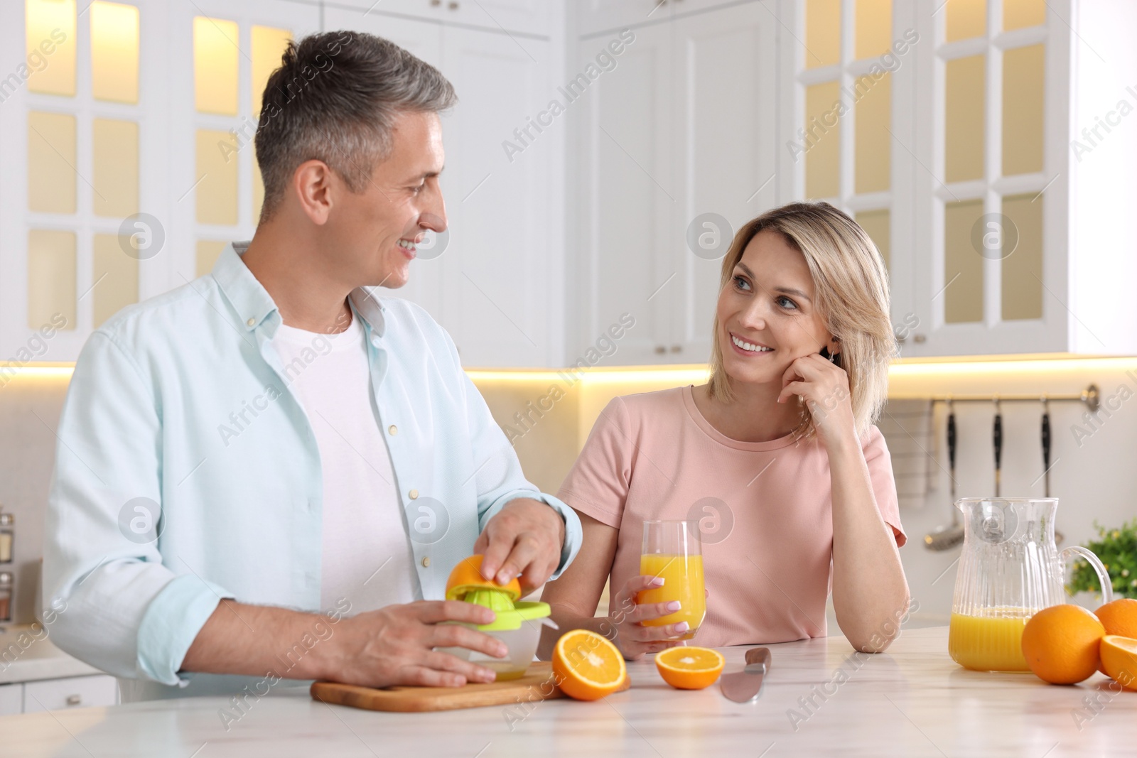 Photo of Happy couple with juicer and fresh products making juice at white marble table in kitchen