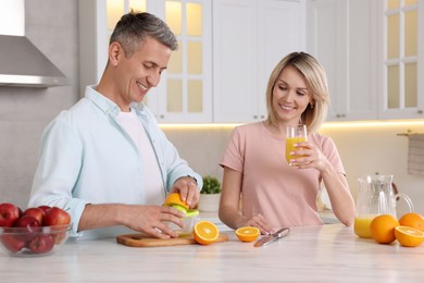 Happy couple with juicer and fresh products making juice at white marble table in kitchen