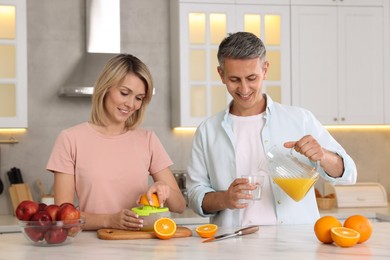 Happy couple with juicer and fresh products making juice at white marble table in kitchen