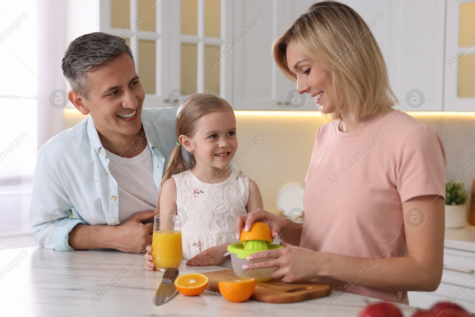 Photo of Happy family with juicer and fresh products making juice at white marble table in kitchen