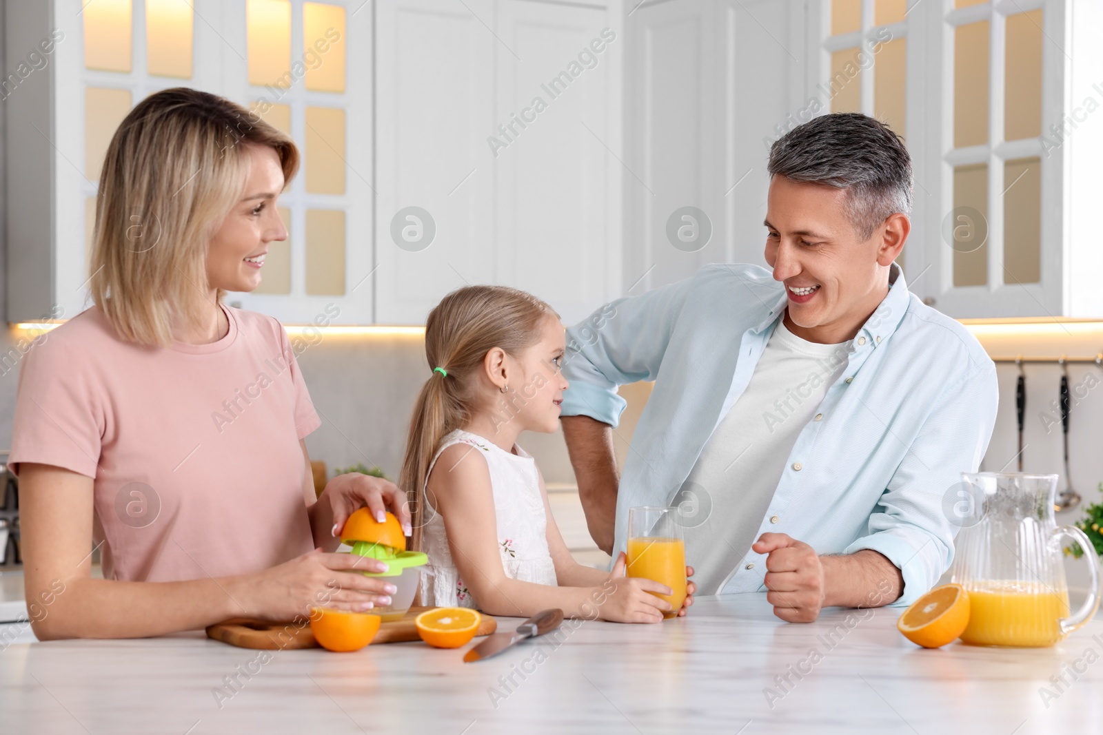 Photo of Happy family with juicer and fresh products making juice at white marble table in kitchen