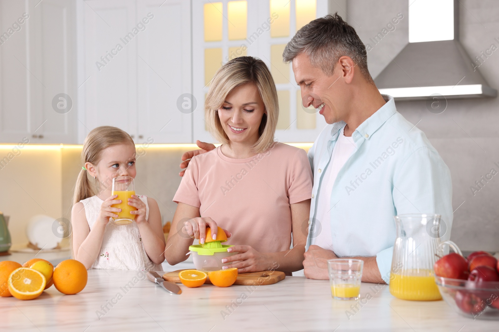 Photo of Happy family with juicer and fresh products making juice at white marble table in kitchen