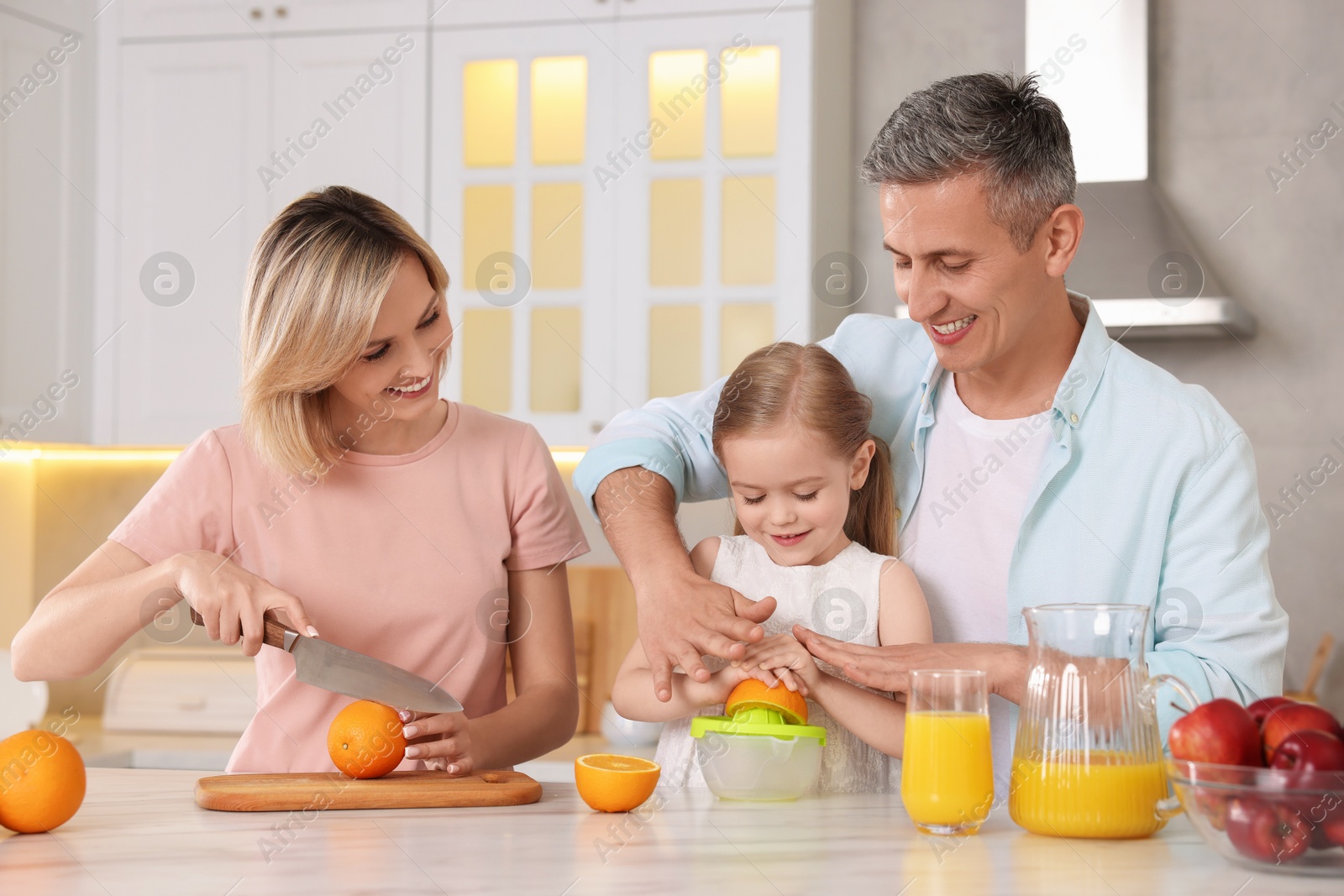 Photo of Happy family making juice at white marble table in kitchen