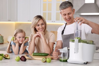 Happy family with juicer and fresh products making drink at white marble table in kitchen