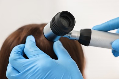 Photo of Trichologist with dermatoscope examining patient`s hair in clinic, closeup