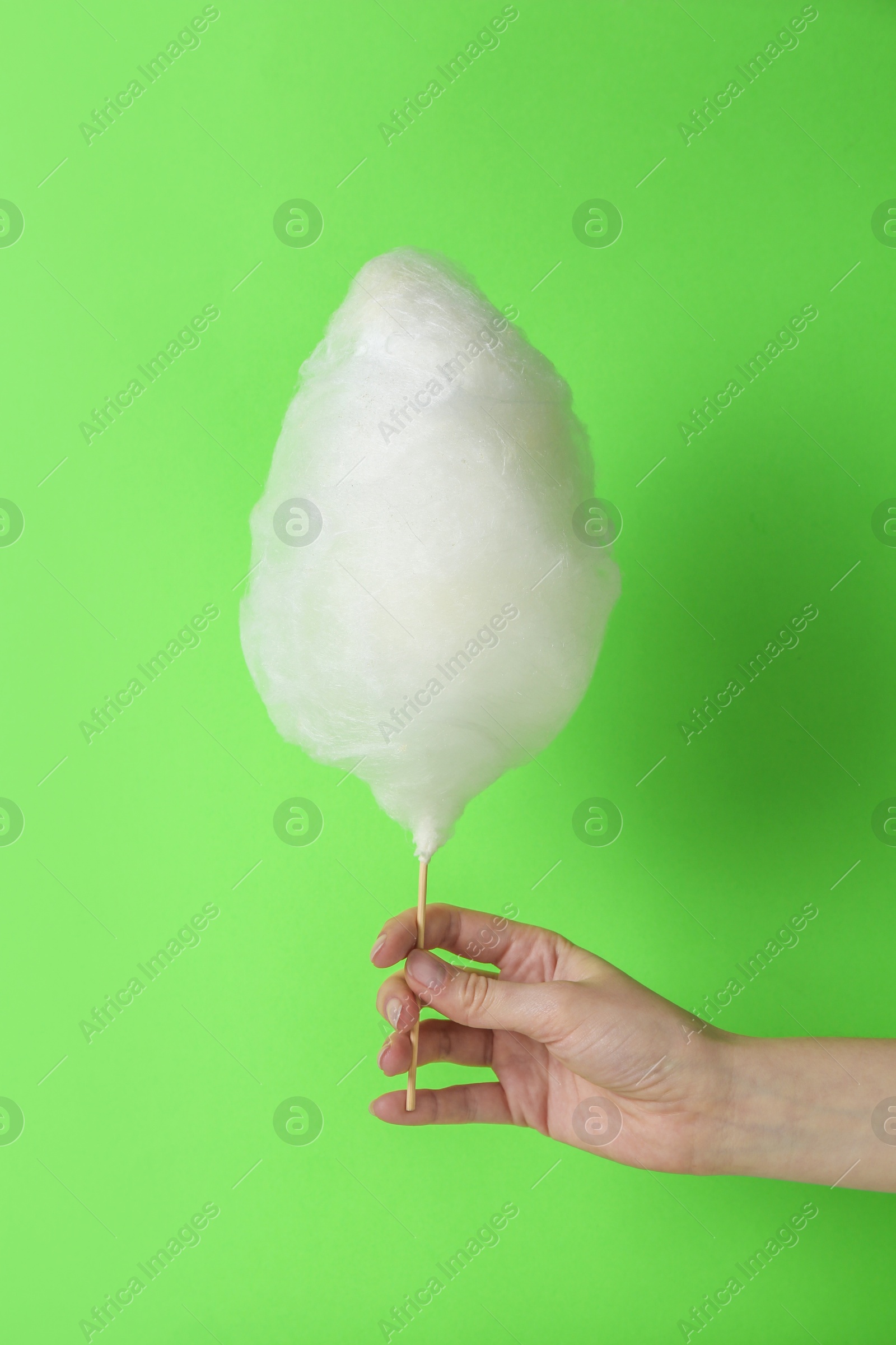 Photo of Woman holding sweet cotton candy on light green background, closeup