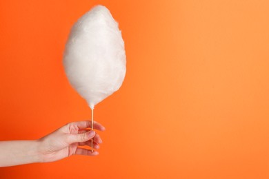 Photo of Woman holding sweet cotton candy on orange background, closeup. Space for text