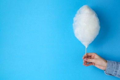 Woman holding sweet cotton candy on light blue background, closeup. Space for text