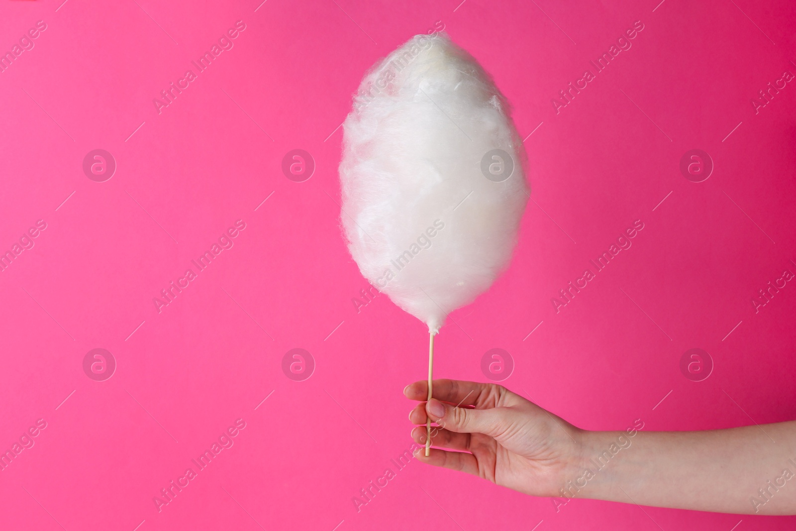 Photo of Woman holding sweet cotton candy on pink background, closeup. Space for text