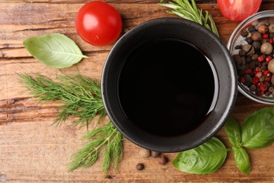 Photo of Balsamic vinegar in bowl, tomatoes, herbs and spices on wooden table, flat lay