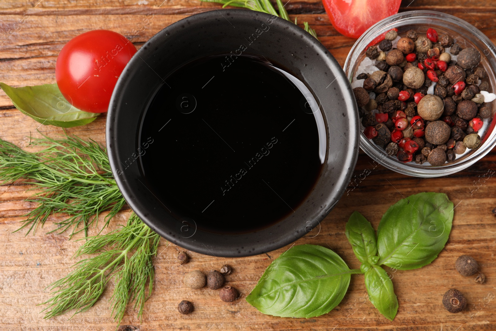 Photo of Balsamic vinegar in bowl, tomatoes, herbs and spices on wooden table, flat lay