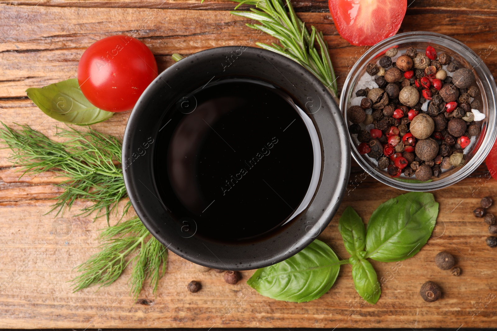 Photo of Balsamic vinegar in bowl, tomatoes, herbs and spices on wooden table, flat lay