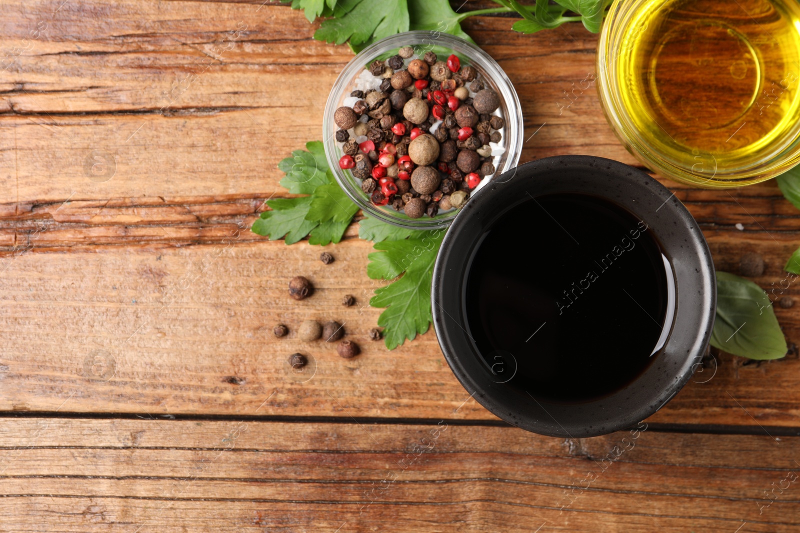 Photo of Balsamic vinegar in bowl, oil, herbs and spices on wooden table, flat lay. Space for text