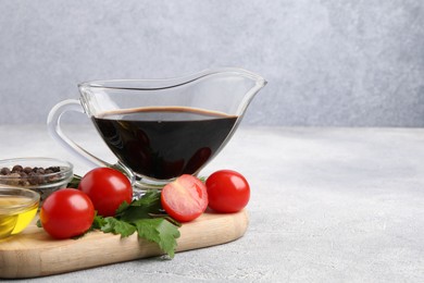 Photo of Balsamic vinegar in gravy boat, oil, tomatoes, parsley and spices on gray textured table, space for text