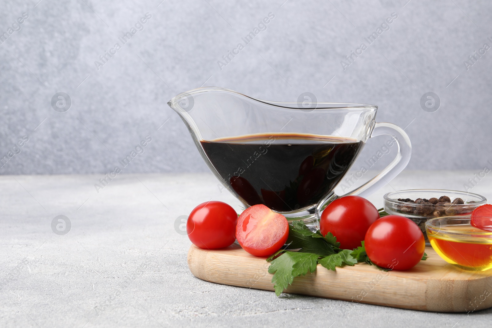 Photo of Balsamic vinegar in gravy boat, oil, tomatoes, parsley and spices on gray textured table, space for text