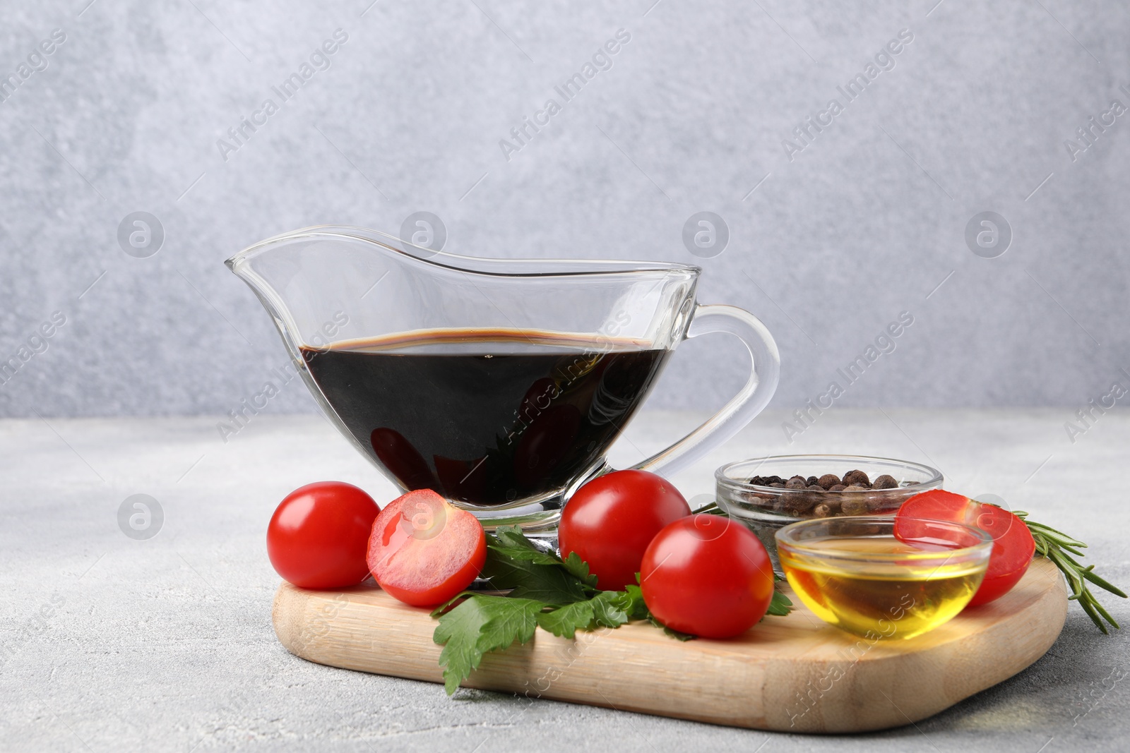 Photo of Balsamic vinegar in gravy boat, oil, tomatoes, herbs and spices on gray textured table