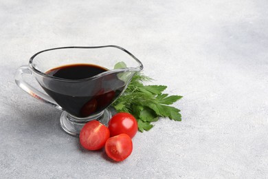 Photo of Balsamic vinegar in gravy boat, tomatoes, parsley and dill on gray textured table, space for text