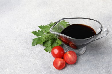 Photo of Balsamic vinegar in gravy boat, tomatoes, parsley and dill on gray textured table, space for text