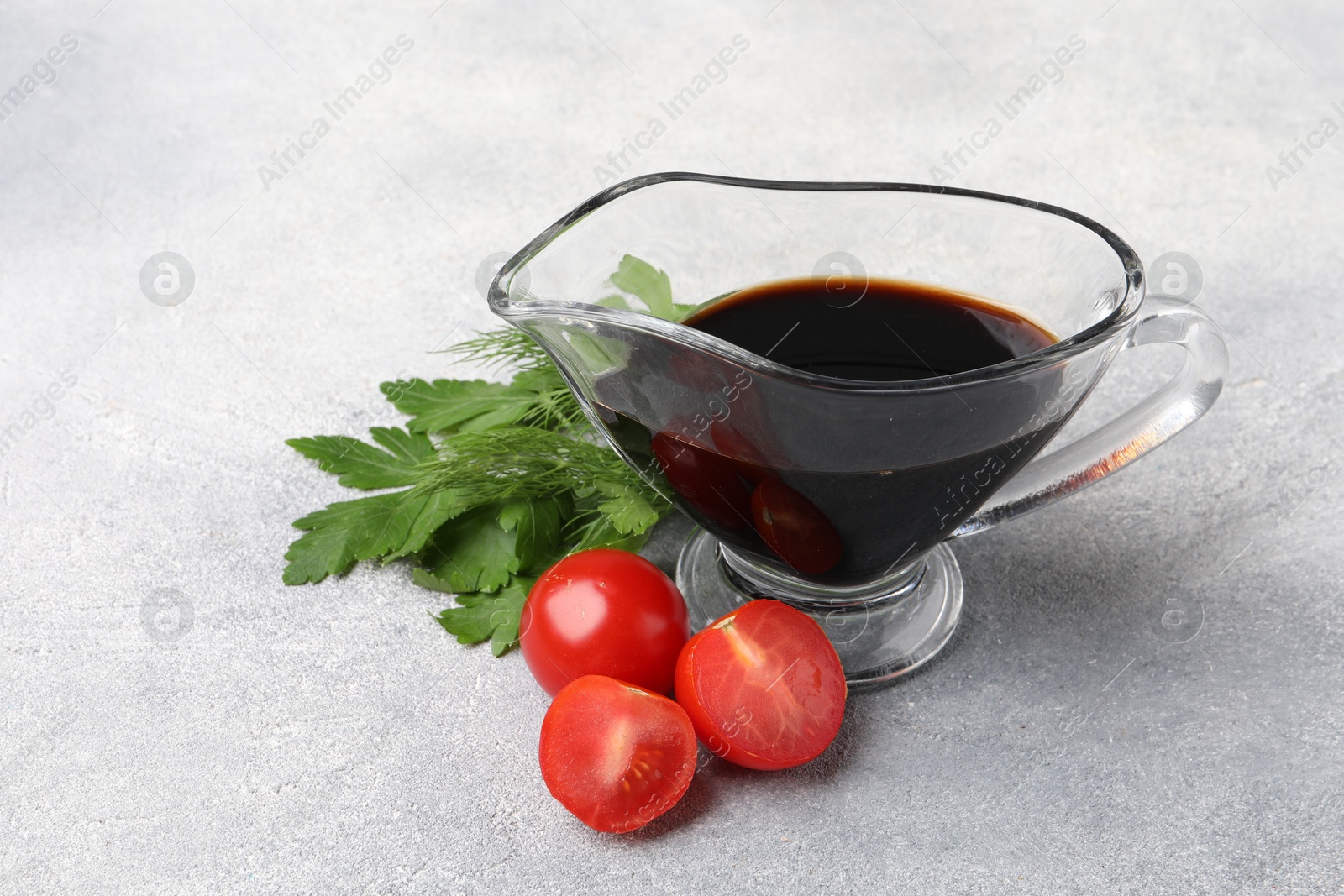 Photo of Balsamic vinegar in gravy boat, tomatoes, parsley and dill on gray textured table