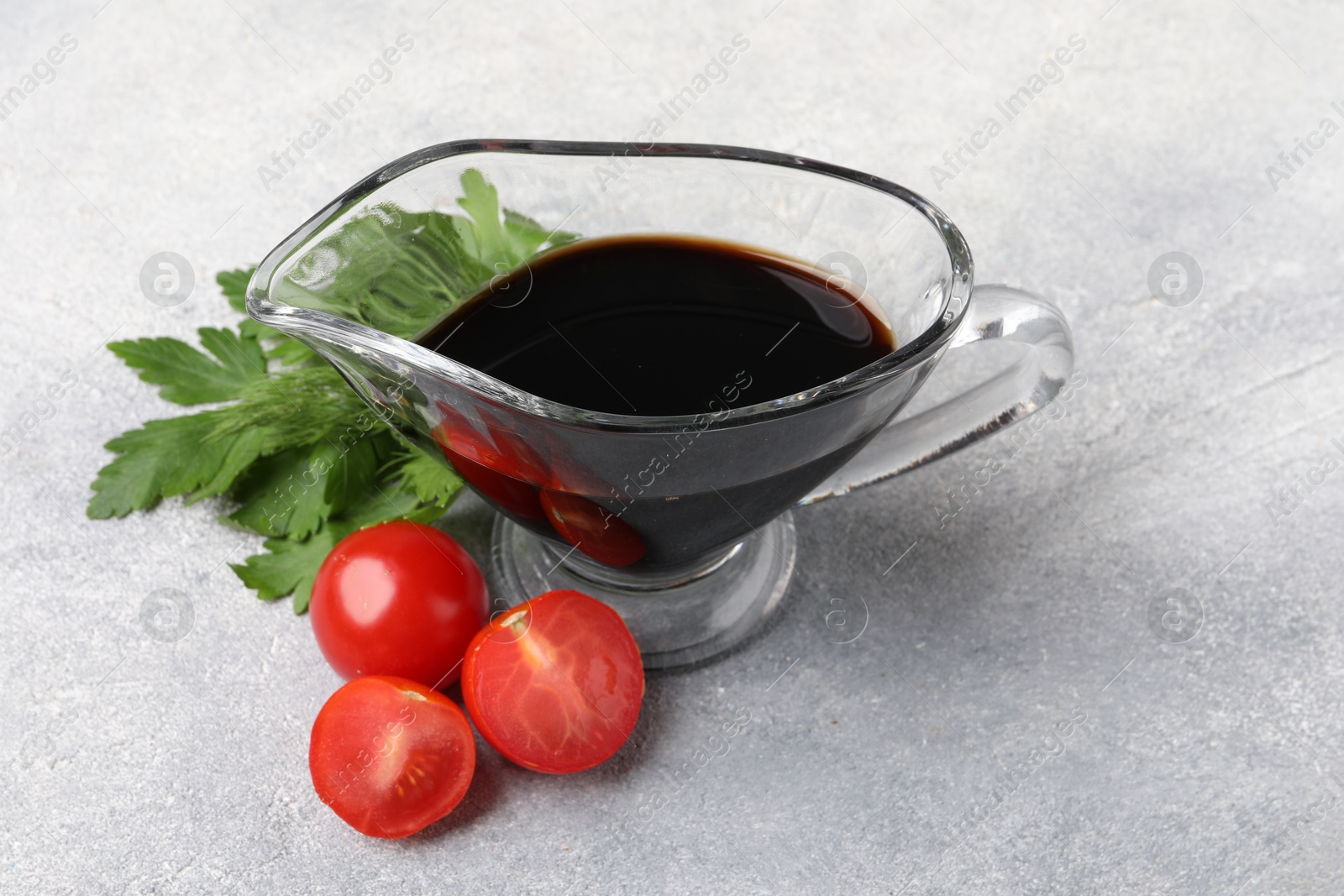 Photo of Balsamic vinegar in gravy boat, tomatoes, parsley and dill on gray textured table