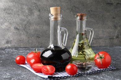 Photo of Balsamic vinegar in glass jug, oil, tomatoes and spices on gray textured table