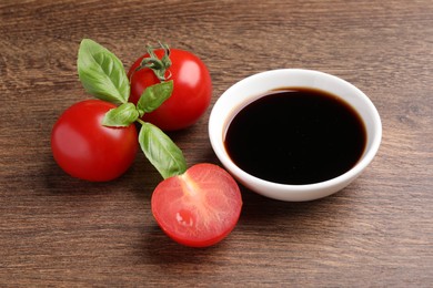 Balsamic vinegar in bowl, basil and tomatoes on wooden table