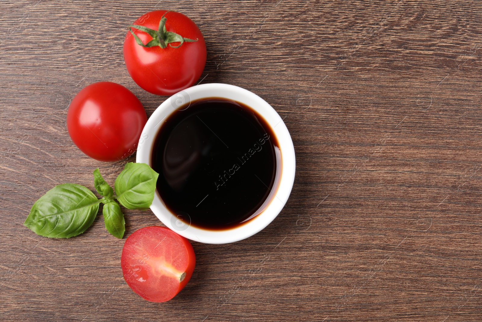 Photo of Balsamic vinegar in bowl, basil and tomatoes on wooden table, flat lay. Space for text