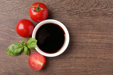 Balsamic vinegar in bowl, basil and tomatoes on wooden table, flat lay. Space for text