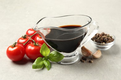 Balsamic vinegar in gravy boat, tomatoes, basil and spices on gray textured table, closeup