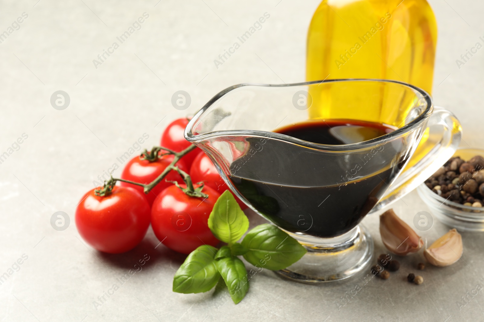 Photo of Balsamic vinegar in gravy boat, oil, tomatoes, basil and spices on gray textured table, closeup