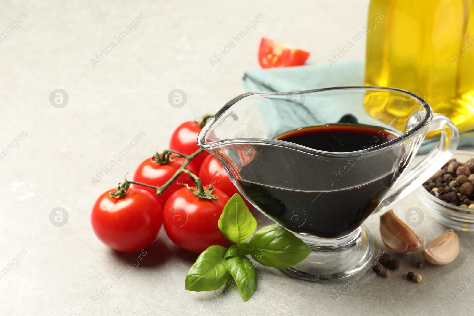 Photo of Balsamic vinegar in gravy boat, oil, tomatoes, basil and spices on gray textured table, closeup