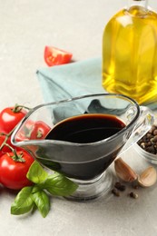 Balsamic vinegar in gravy boat, oil, tomatoes, basil and spices on gray textured table, closeup