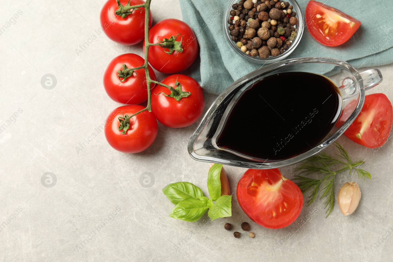 Photo of Balsamic vinegar in gravy boat, tomatoes, herbs and spices on gray textured table, flat lay. Space for text