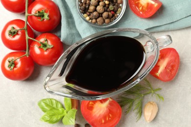 Photo of Balsamic vinegar in gravy boat, tomatoes, herbs and spices on gray textured table, flat lay