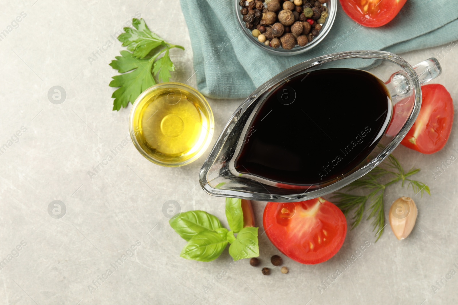 Photo of Balsamic vinegar in gravy boat, oil, tomatoes, herbs and spices on gray textured table, flat lay. Space for text