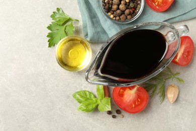 Balsamic vinegar in gravy boat, oil, tomatoes, herbs and spices on gray textured table, flat lay. Space for text