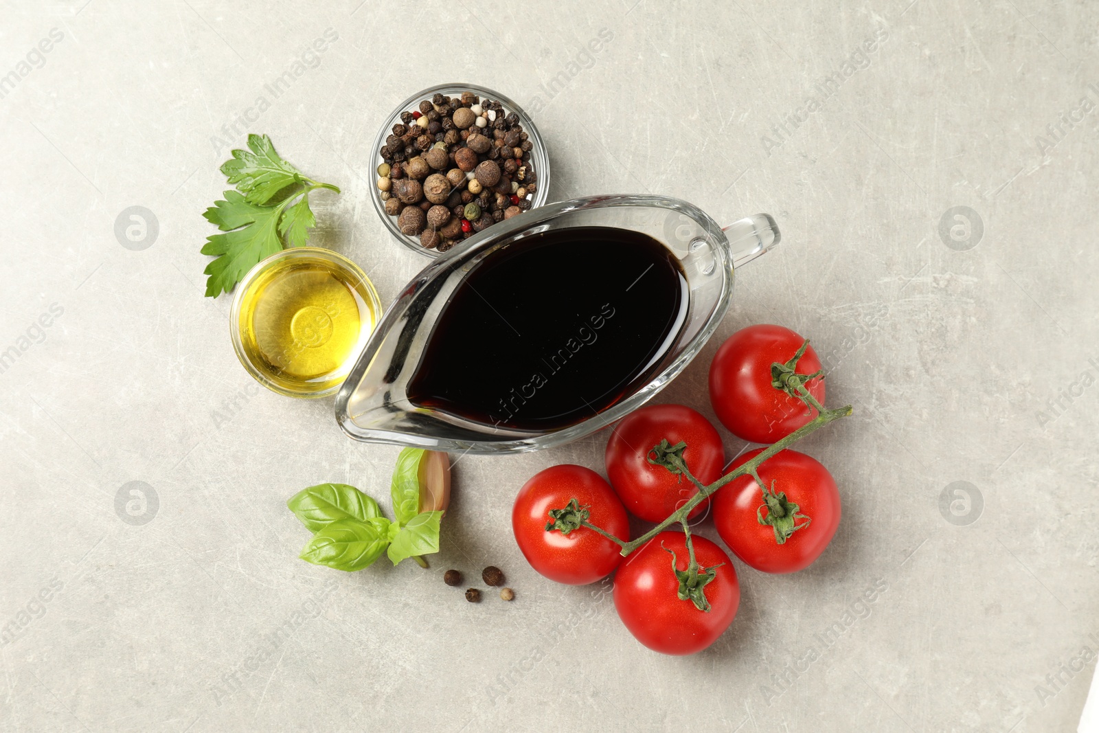 Photo of Balsamic vinegar in gravy boat, oil, tomatoes, herbs and spices on gray textured table, flat lay