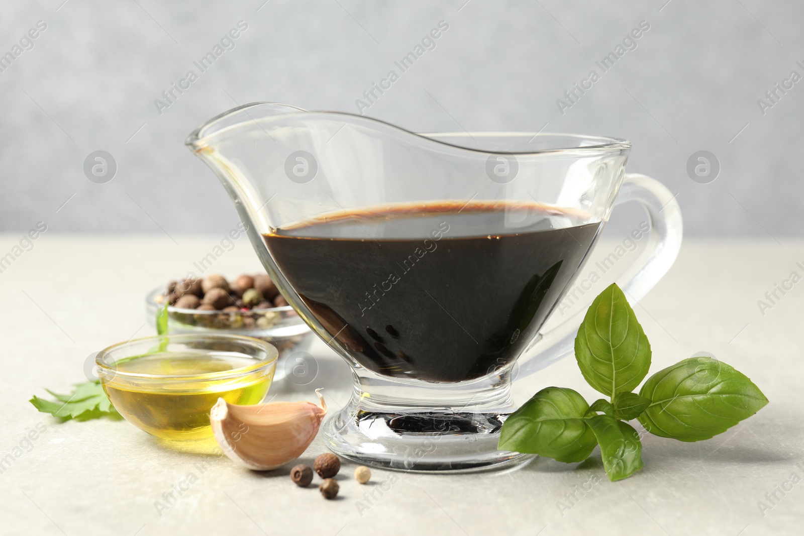 Photo of Balsamic vinegar in gravy boat, oil, basil and spices on gray textured table, closeup